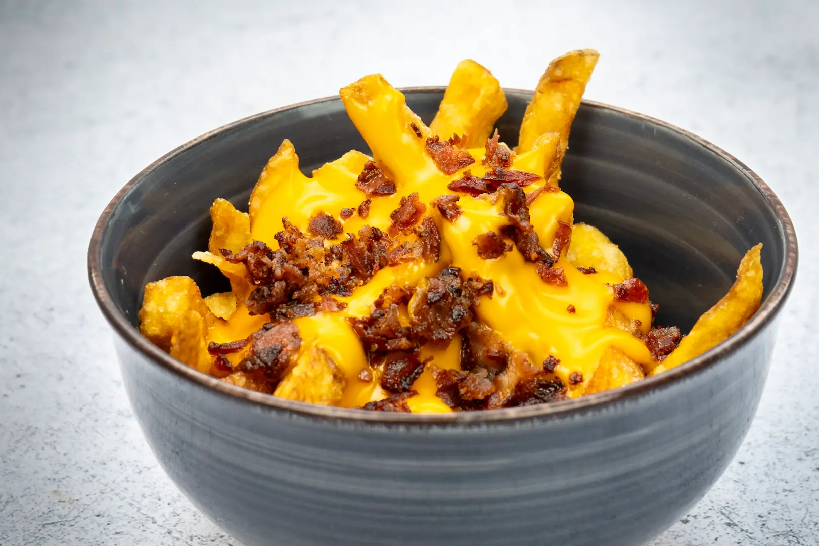 Photographie culinaire couleur de frites jaunes contrastées dans un bol noir